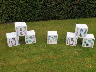 We are selling our laser cut wooden Mrs & Mrs boxes (of course you could use as Mr & Mrs, mr & Mr). Each box is 30 x 30 x30 cm in size, light weight and can easily be painted to any colour you wish. The tops can be removed to fill with coloured sashes or balloons of your choice. These make a lovely feature on stage, to fill a corner stacked or laid out in an outdoor display like shown in the photos.
This is our display set and ready painted in white. We sell these flat pack normally at £40 per letter. We are selling this set of 7 boxes for £110. Collection only from Swinton S64 8AE.